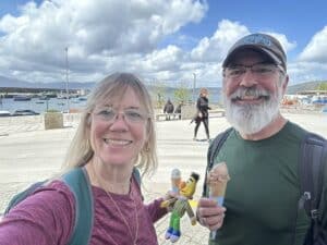Philip and Laura smiling on a waterfront promenade while holding gelato cones, with a small Bert doll between them.