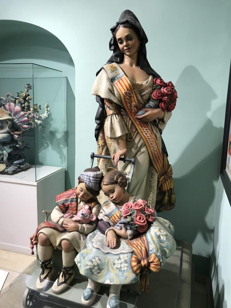 Colorful ninot figure of a Fallera woman with children on display at the Fallas Museum, a unique cultural stop among the top things to do in Valencia.
