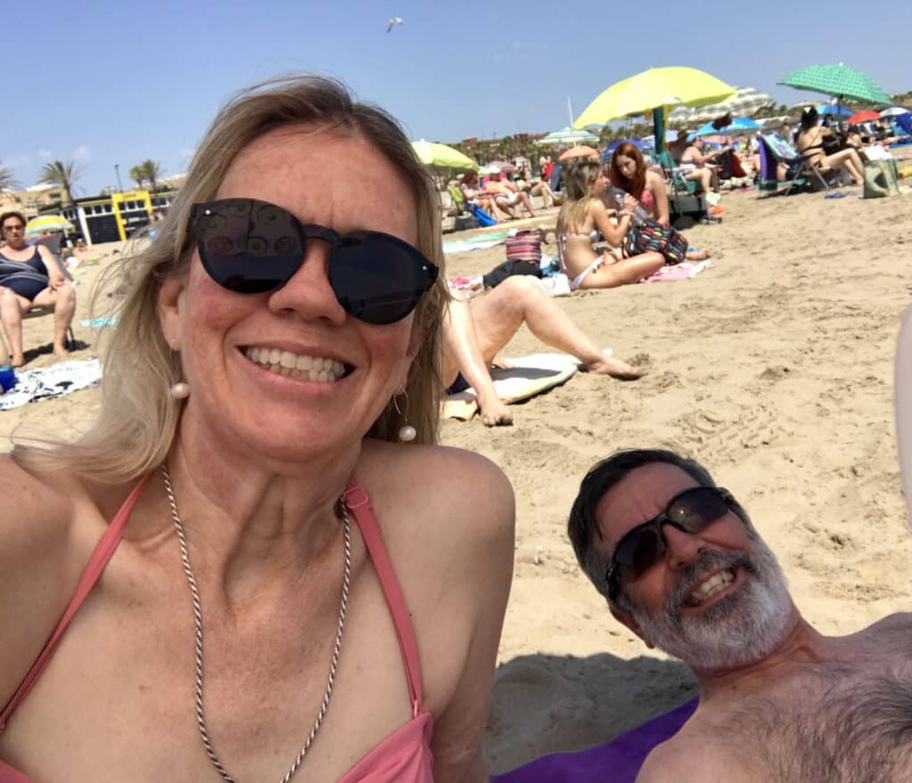 A couple smiling and relaxing on the sand at Malvarrosa Beach in Valencia on a sunny day.