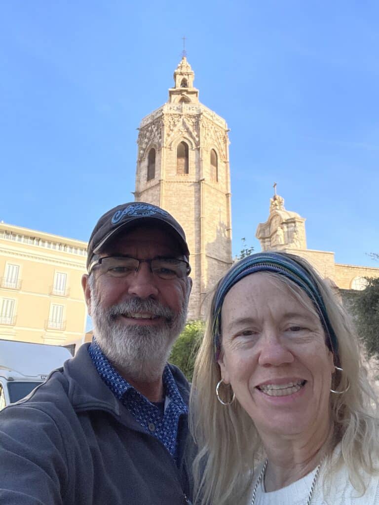 Two travelers smiling in Plaza de la Reina with Valencia’s Miguelete Tower rising behind them, a popular stop among the top things to do in Valencia.