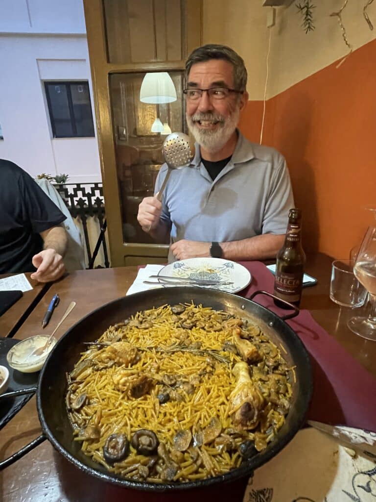 Traveler smiling during a Valencian cooking class with a large pan of fideuà on the table, a popular culinary experience among the top things to do in Valencia.